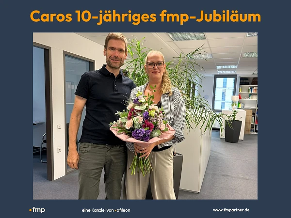 Auf dem Bild sieht man zwei Personen. Markus übergibt Caro einen Blumenstrauß anlässlich ihres 10-jährigen Jubiläums bei fmp