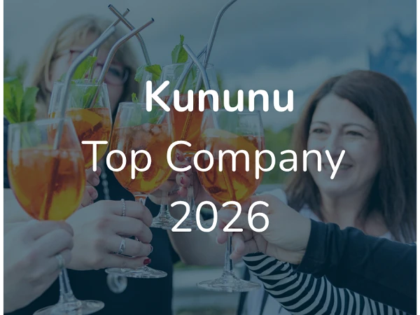 Mehrere Menschen stoßen mit Gläsern voller Getränke an, während im Vordergrund die Aufschrift „Kununu Top Company 2026“ zu sehen ist.